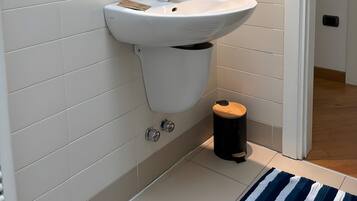 A bathroom with a white sink, a mirror, and a small trash bin.