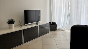 Un salon moderne avec un téléviseur à écran plat, une plante en pot et un pouf noir.