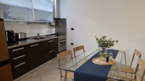 Une cuisine moderne avec des meubles de couleur sombre, une hotte de cuisine en acier inoxydable et une table à manger en verre, assortie de chaises.