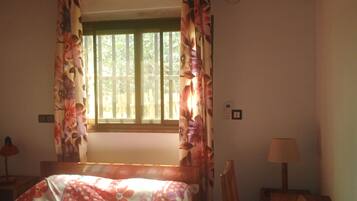 Een kamer met een bed, een raam met gordijnen, een airconditioningsunit, een bureau met lamp en een stoel.