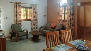 Ein gemütliches Wohnzimmer mit einer Couch, Sesseln, einem Holztisch und einem Esstisch mit Platzsets.
