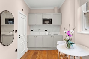 Une cuisine moderne avec des meubles blancs, un four à micro-ondes, un évier et une table blanche agrémentée d’un vase de fleurs.