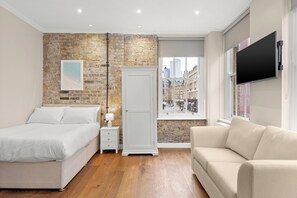 Een slaapkamer met een bed, een nachtkastje, een dressoir, een raam met uitzicht over de stad en een aan de muur bevestigde televisie.
