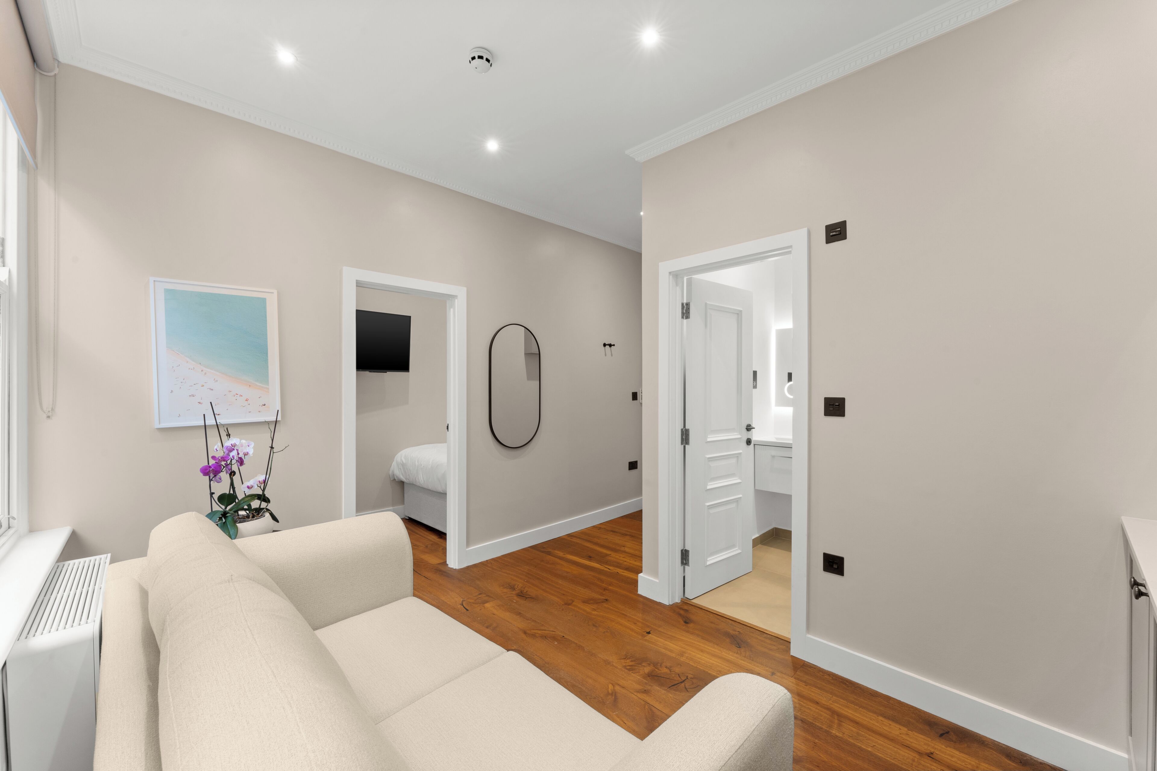 A modern interior with a sofa, a flat-screen TV, a bathroom with a toilet and sink, and a hallway leading to another room.