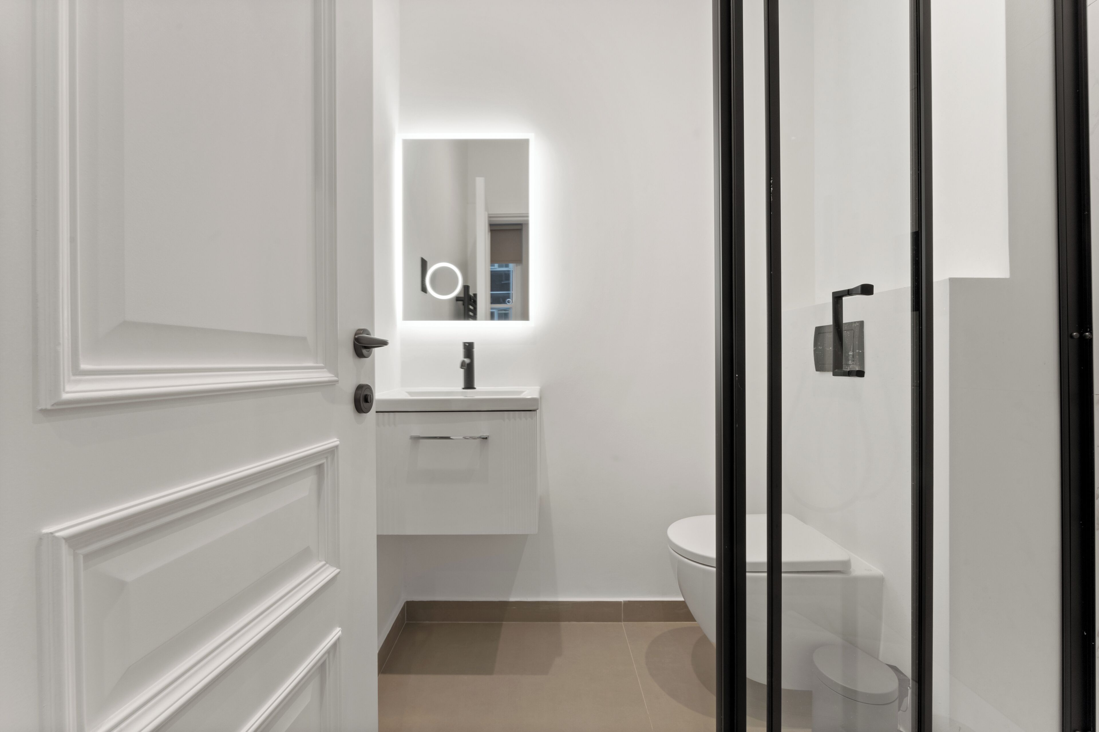 Une salle de bain moderne avec un meuble-lavabo blanc, un miroir avec éclairage intégré, des toilettes et une douche à parois de verre.