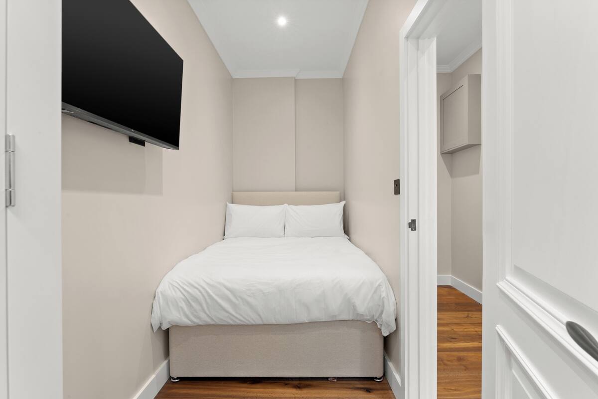 A bedroom with a bed, a flat-screen TV mounted on the wall, and a wooden floor.