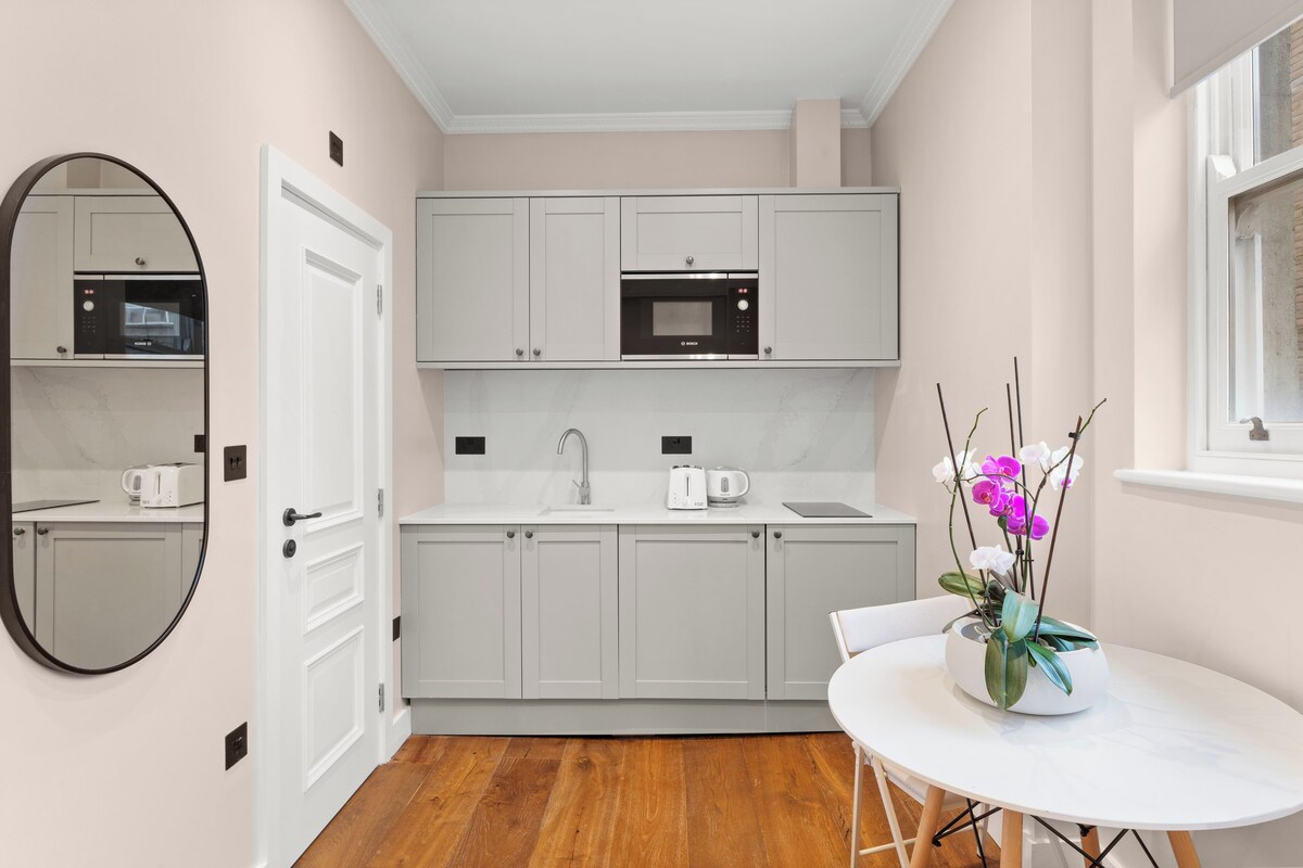 A modern kitchen with white cabinets, a microwave, a sink, and a white table with a flower vase.
