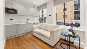 A modern kitchen with grey cabinets, a white countertop, and a beige sofa. - Grove Heights Shoreditch  (London)
