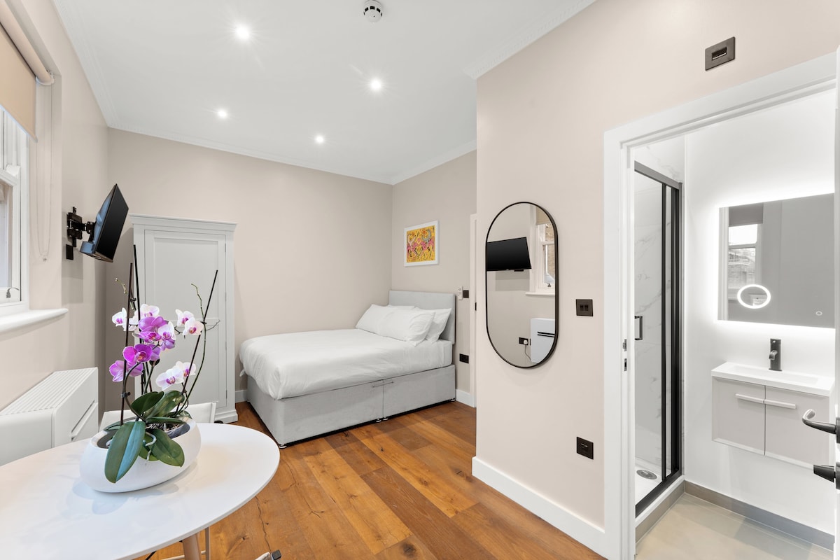 A modern bedroom with a bed, a round mirror, a white bedside table, and a potted orchid.