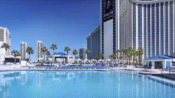 A pool area with lounge chairs and umbrellas, surrounded by tall buildings and palm trees. - 1BR, 1BA SUITE WITH FULL KITCHEN AMENITIES 5 MIN FROM STRIP SLEEPS 6 (Las Vegas)