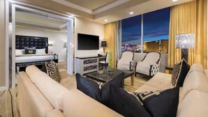 A modern hotel room with a large bed, a seating area with sofas and a coffee table, a TV, and a city view through the window. - 1BR, 1BA SUITE WITH FULL KITCHEN AMENITIES 5 MIN FROM STRIP SLEEPS 6 (Las Vegas)
