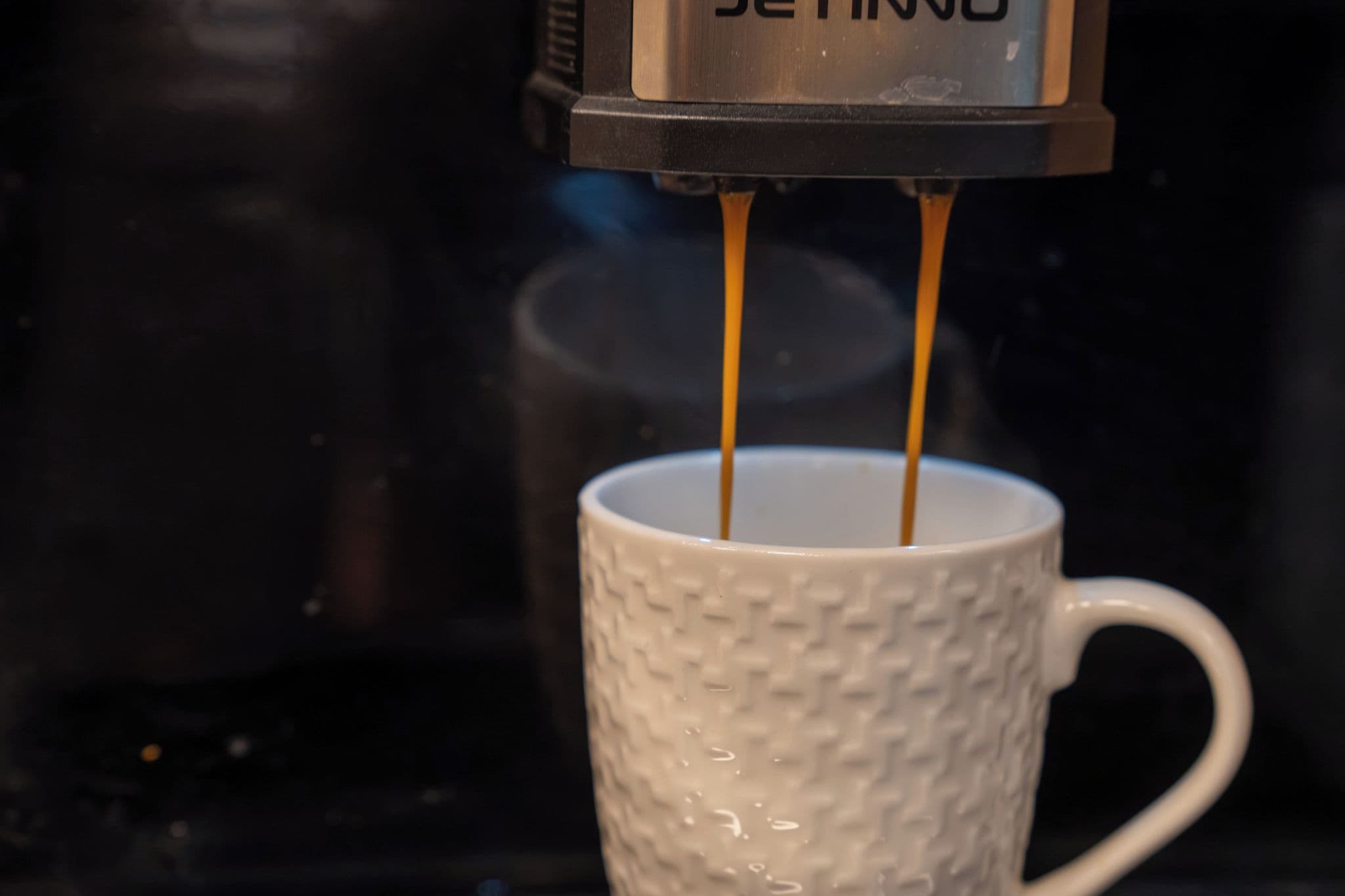 En kaffemaskine tapper kaffe i en hvid kop.
