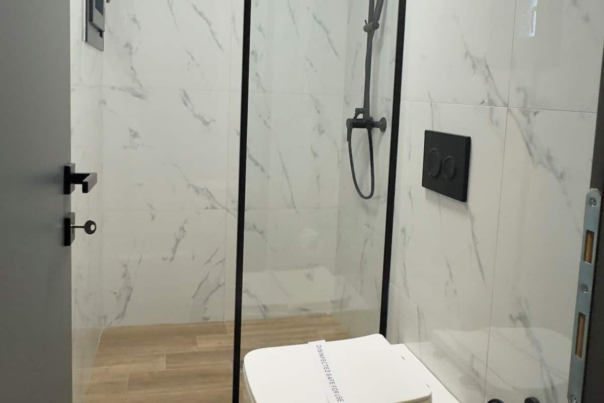 Une salle de bain moderne avec une douche à parois de verre, des toilettes et une poubelle.