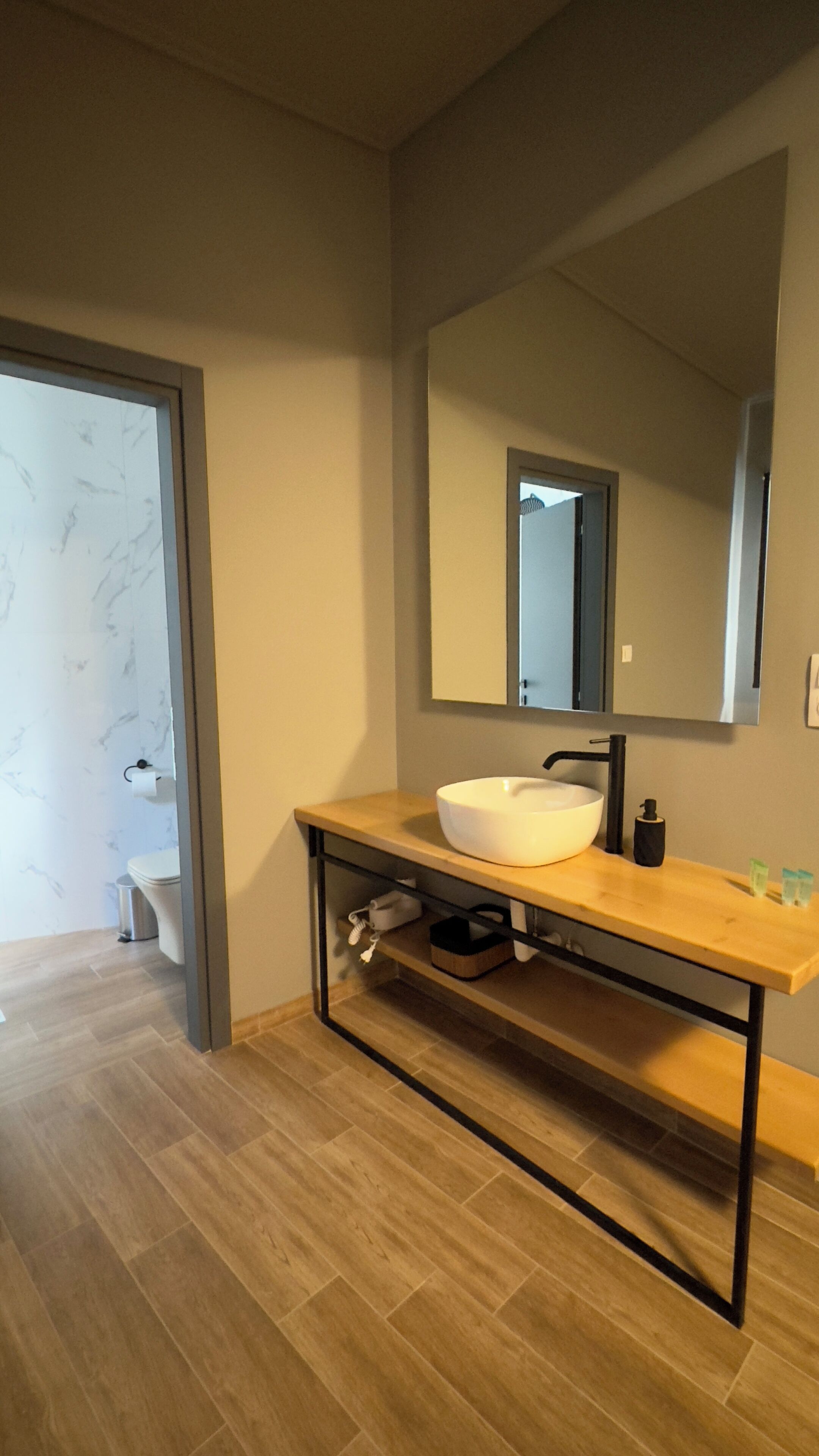 Un baño moderno con un lavabo blanco, un espejo grande y un mueble de tocador de madera.
