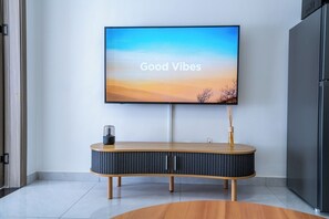 A modern living room with a flat-screen TV displaying 'Good Vibes' on the wall, a wooden console table with a vase, and a sleek black cabinet. - Modern Apartment in Westlands close to Sarit and GTC (Nairobi)