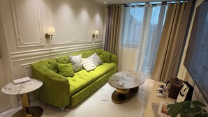 A modern living room with a green sofa, marble flooring, a chandelier, and a TV. - Azure Resort 2BR Deluxe Beach & Pool View with Bathtub • 8 Pax • Smart Toilet (Parañaque)