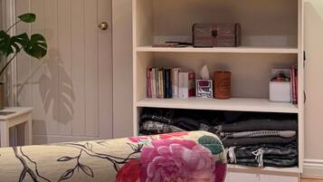 Ein Wohnzimmer mit an der Wand montiertem Fernseher, einer Bücherwand, einer Lampe und einem blumengemusterten Sessel.