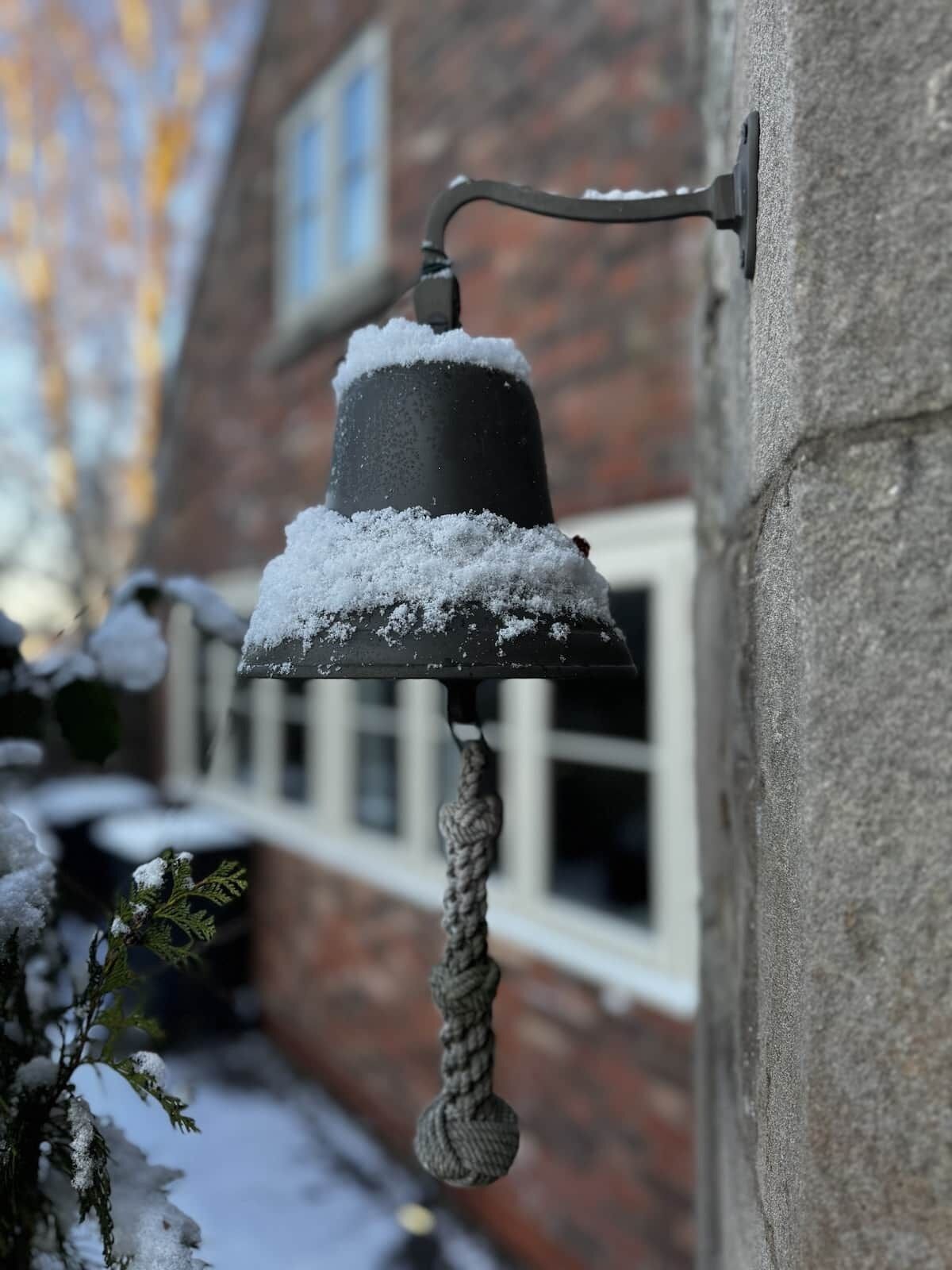 En snötäckt utomhusklocka som är fäst på en byggnadsvägg.