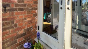 A brick exterior wall with a glass door, a small potted plant, and a doorbell.