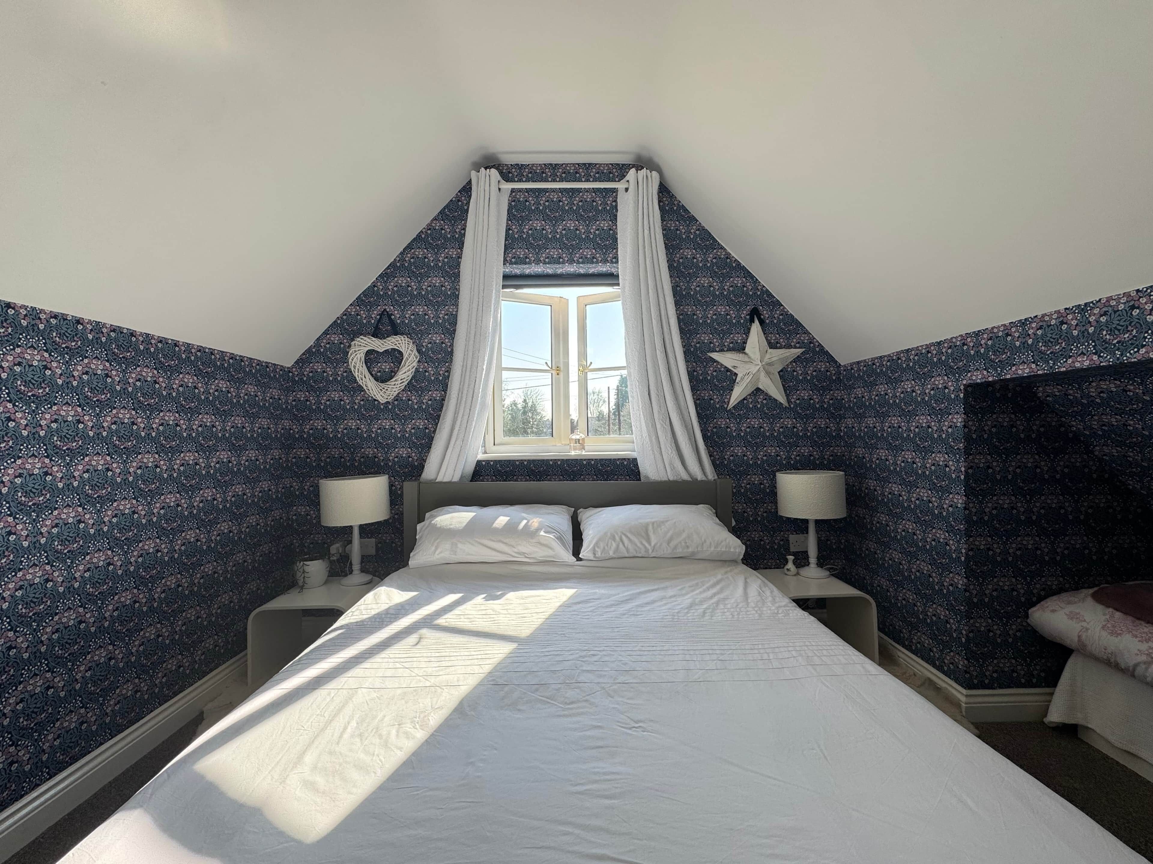 Ein Schlafzimmer mit Bett, zwei Nachttischen, einem Fenster mit Vorhängen, einer Stern-Dekoration und einem herzförmigen Wandbild.