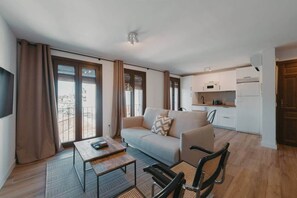 Een moderne woonkamer met een bank, salontafel en stoelen. Het heeft ook een keukenhoek met kastjes en een magnetron.