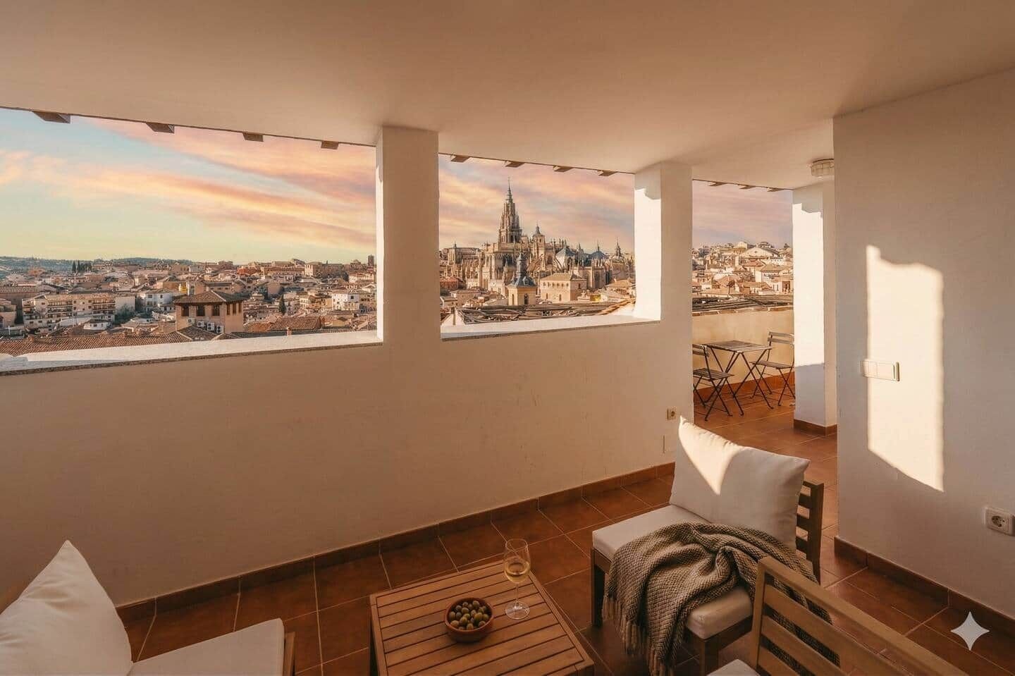 Un balcón con vistas a la ciudad, una mesa con un bol y un vaso, y una silla.
