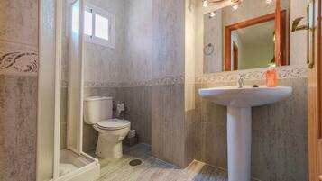 Een badkamer met douche, toilet, wastafel en spiegel.