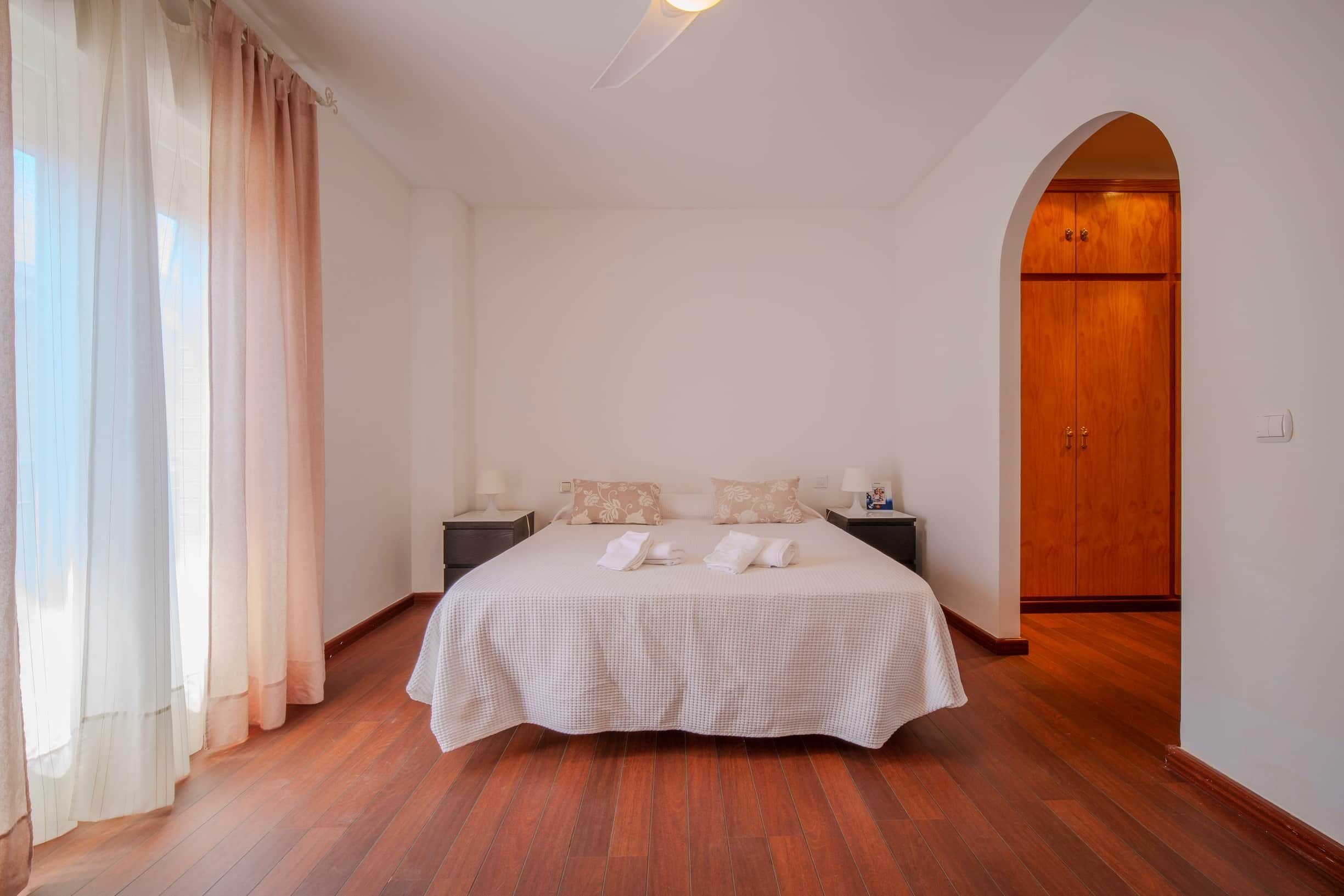 A bedroom with a large bed, two bedside tables, a wooden wardrobe, and a window with curtains.