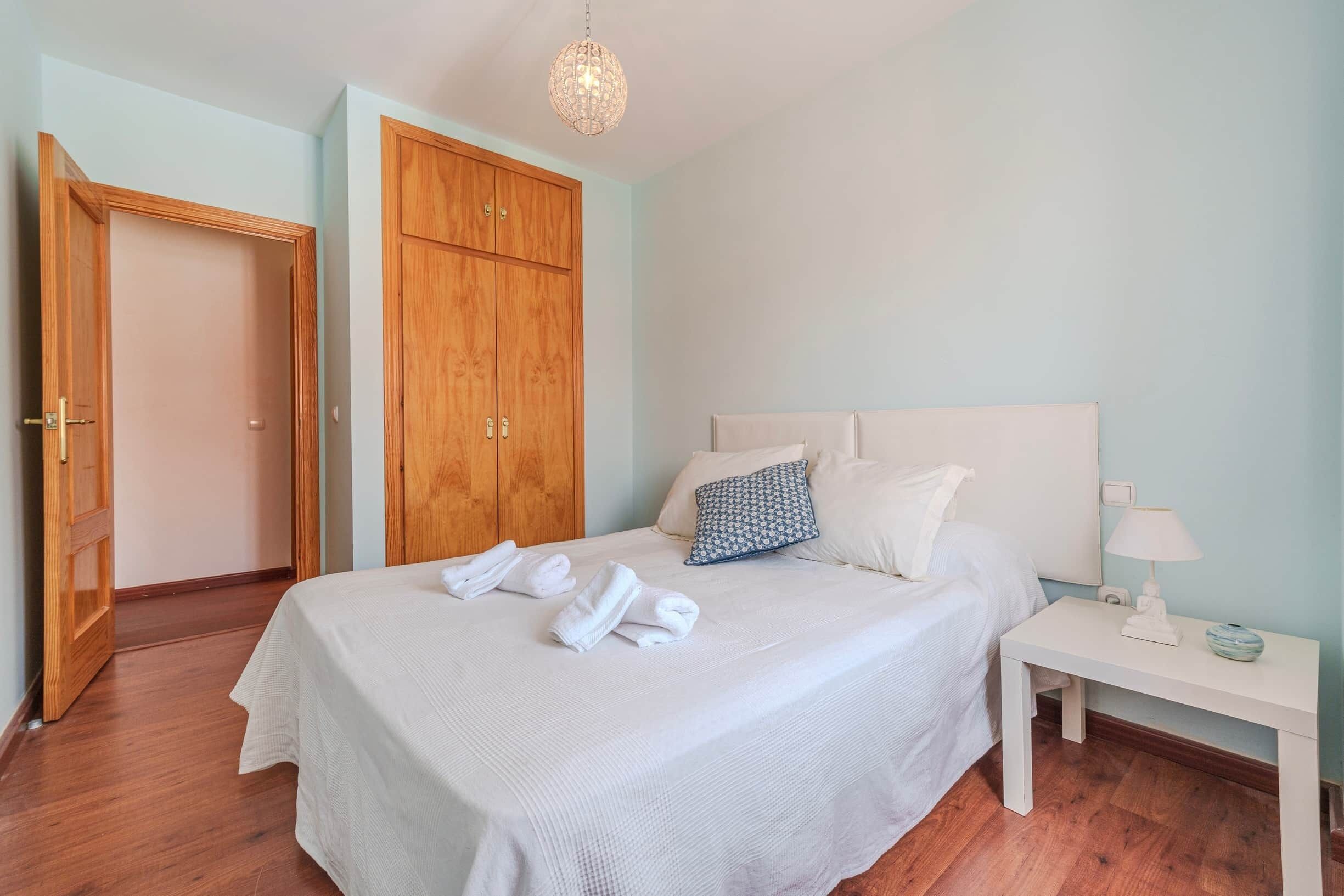 Un dormitorio con una cama, una mesita de noche, un armario de madera y una puerta.