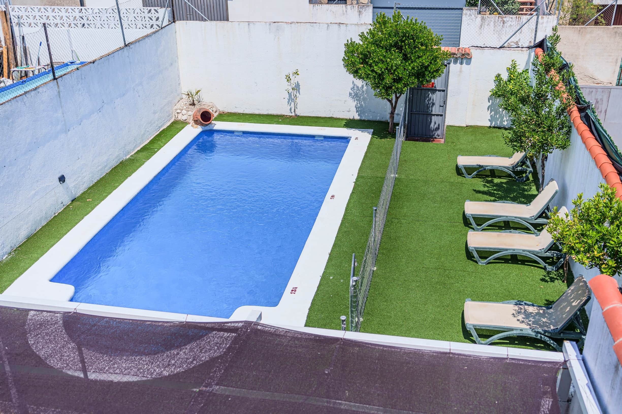 A rectangular pool with a white edge, surrounded by artificial grass and a few trees.