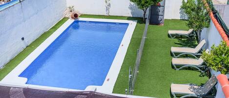 A rectangular pool with a white edge, surrounded by artificial grass and a few trees.