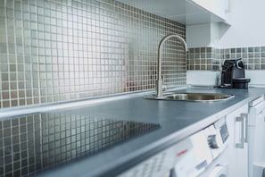 Een moderne keuken met een rvs-spoelbak, betegelde achterwand en een koffieapparaat.