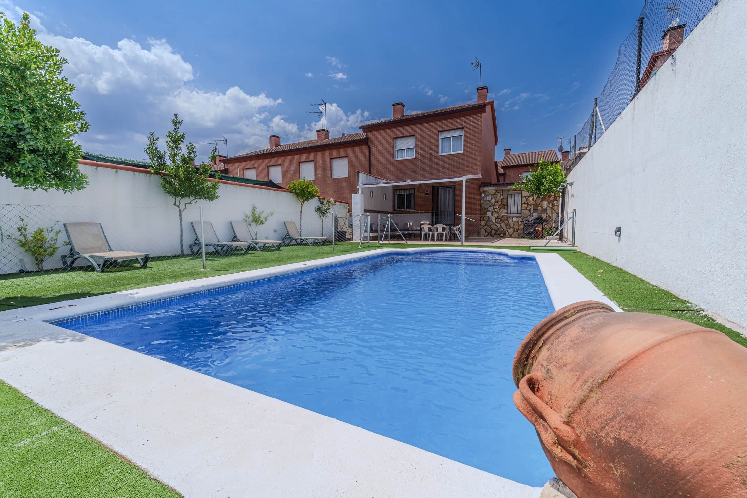 Una piscina rectangular con borde blanco, rodeada por un césped y una pared blanca.