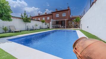 Una piscina rectangular con borde blanco, rodeada por un césped y una pared blanca.