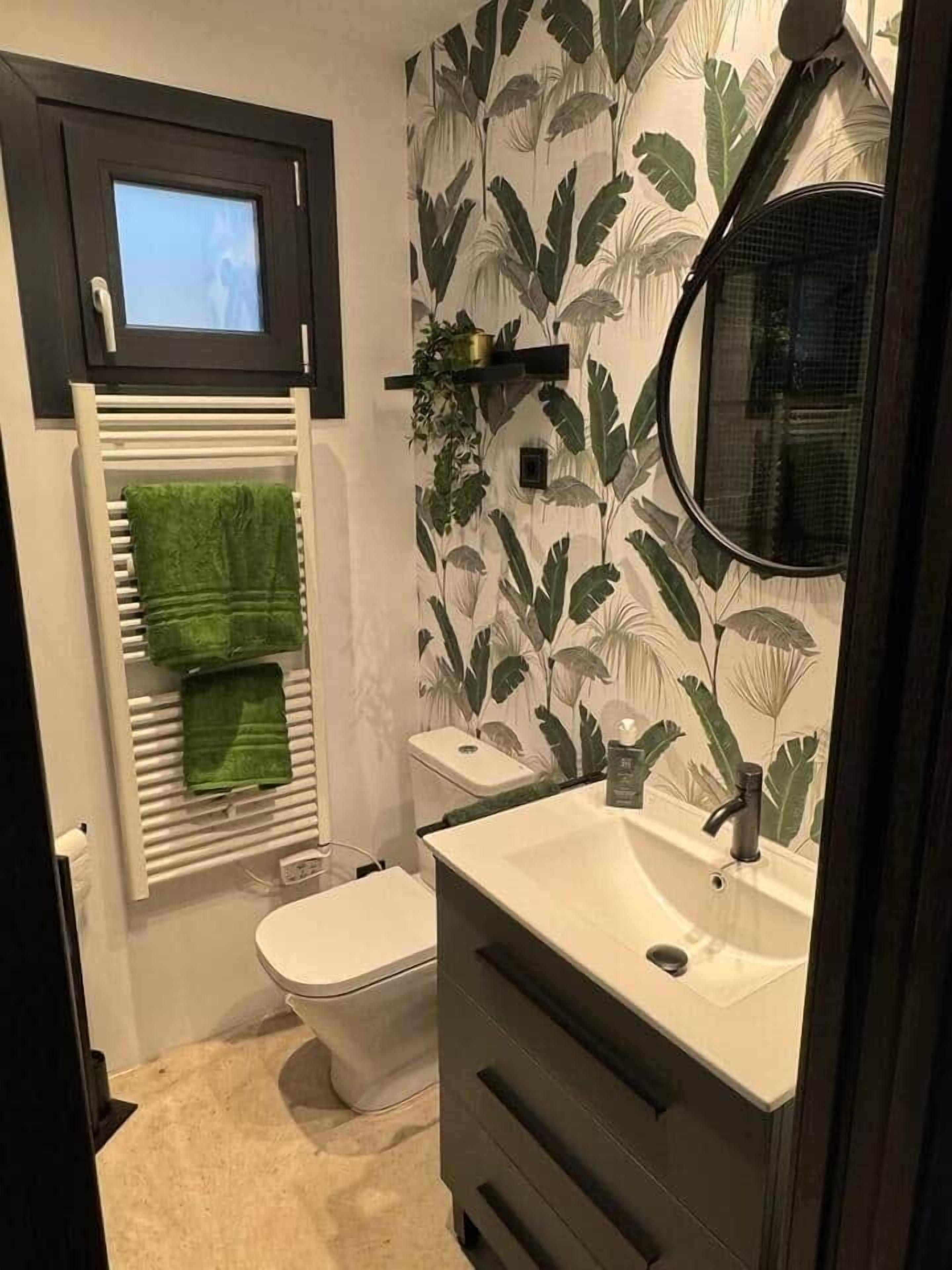 A bathroom with a toilet, a sink, a mirror, and a towel rack with green towels.