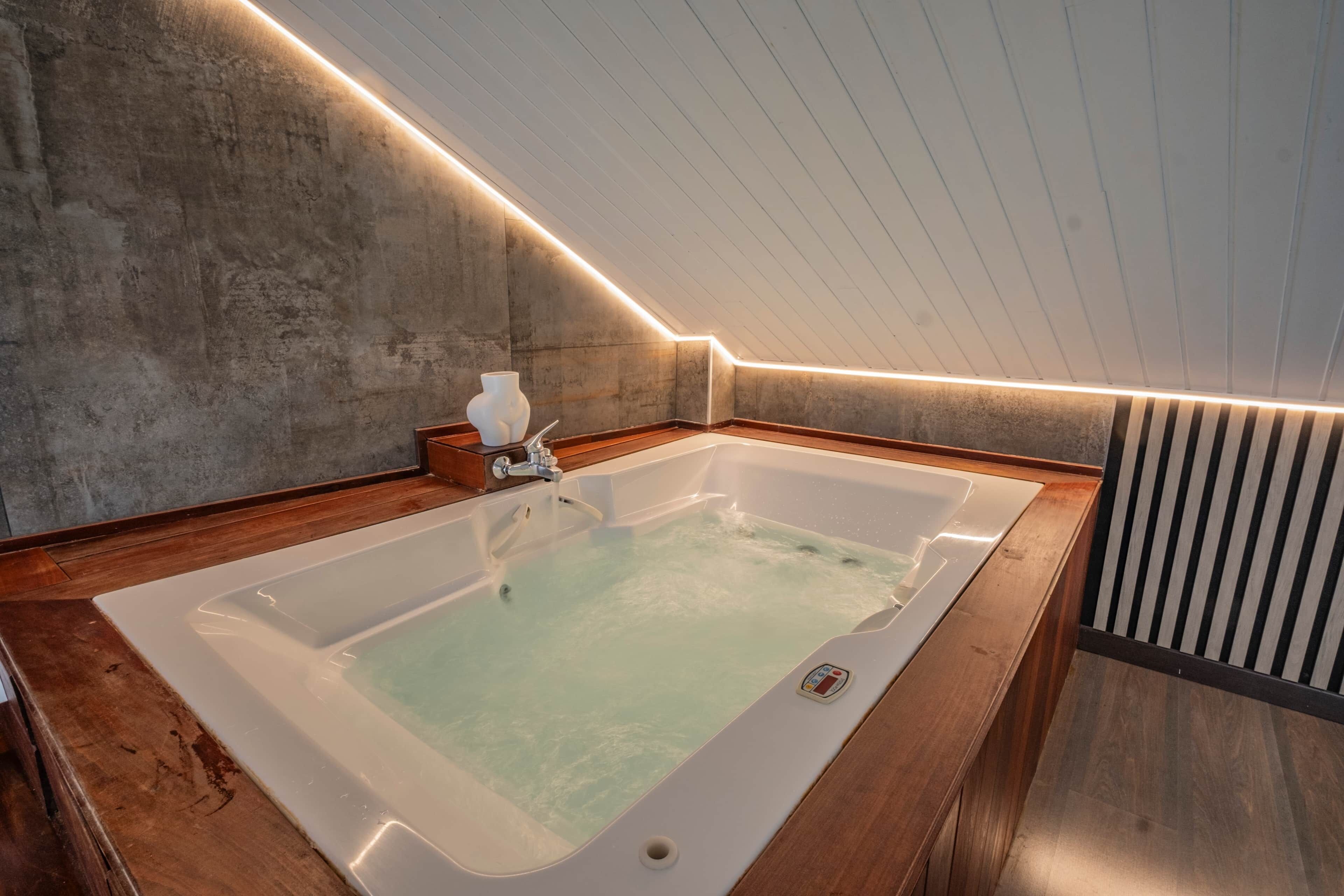 A modern bathroom with a large bathtub, wooden flooring, and a sloped ceiling.