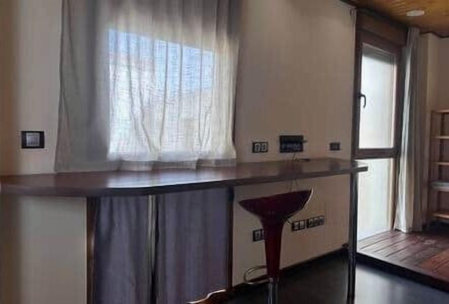 A modern kitchen with a wooden countertop, a built-in oven, and a window with sheer curtains.