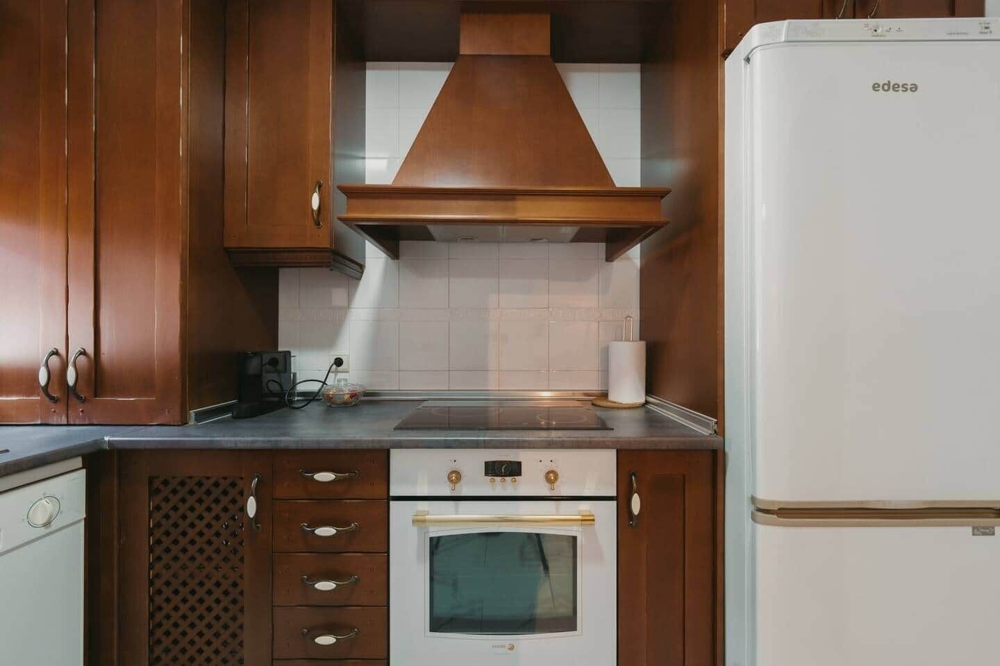 A kitchen with wooden cabinets, a built-in oven, a stove, and a white refrigerator.