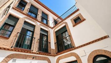 Un edificio de varios pisos con patio central, que presenta balcones con barandillas negras, ventanas de arco y una combinación de fachadas de ladrillo y enlucido.
