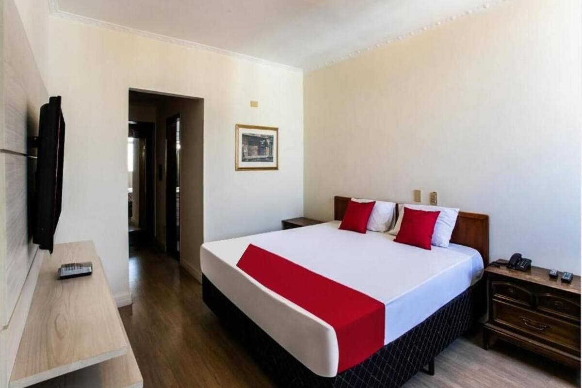 Una camera d'albergo con un letto grande, un comodino, una TV e un settimino in legno.