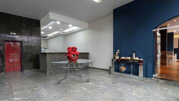 A hotel lobby with a reception desk, a red flower vase, a coffee station, and a dark blue accent wall.