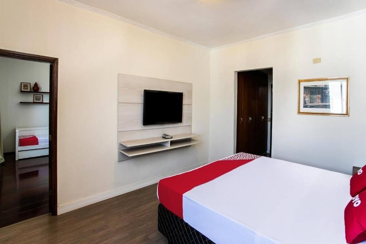Una camera d'albergo con un letto, una televisione a muro, una porta e un quadro incorniciato.