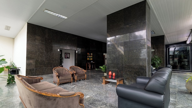 A lobby with a black leather sofa, two brown armchairs, a coffee table, and a reception desk.