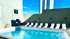 A swimming pool with lounge chairs, a stone deck, and a building in the background.