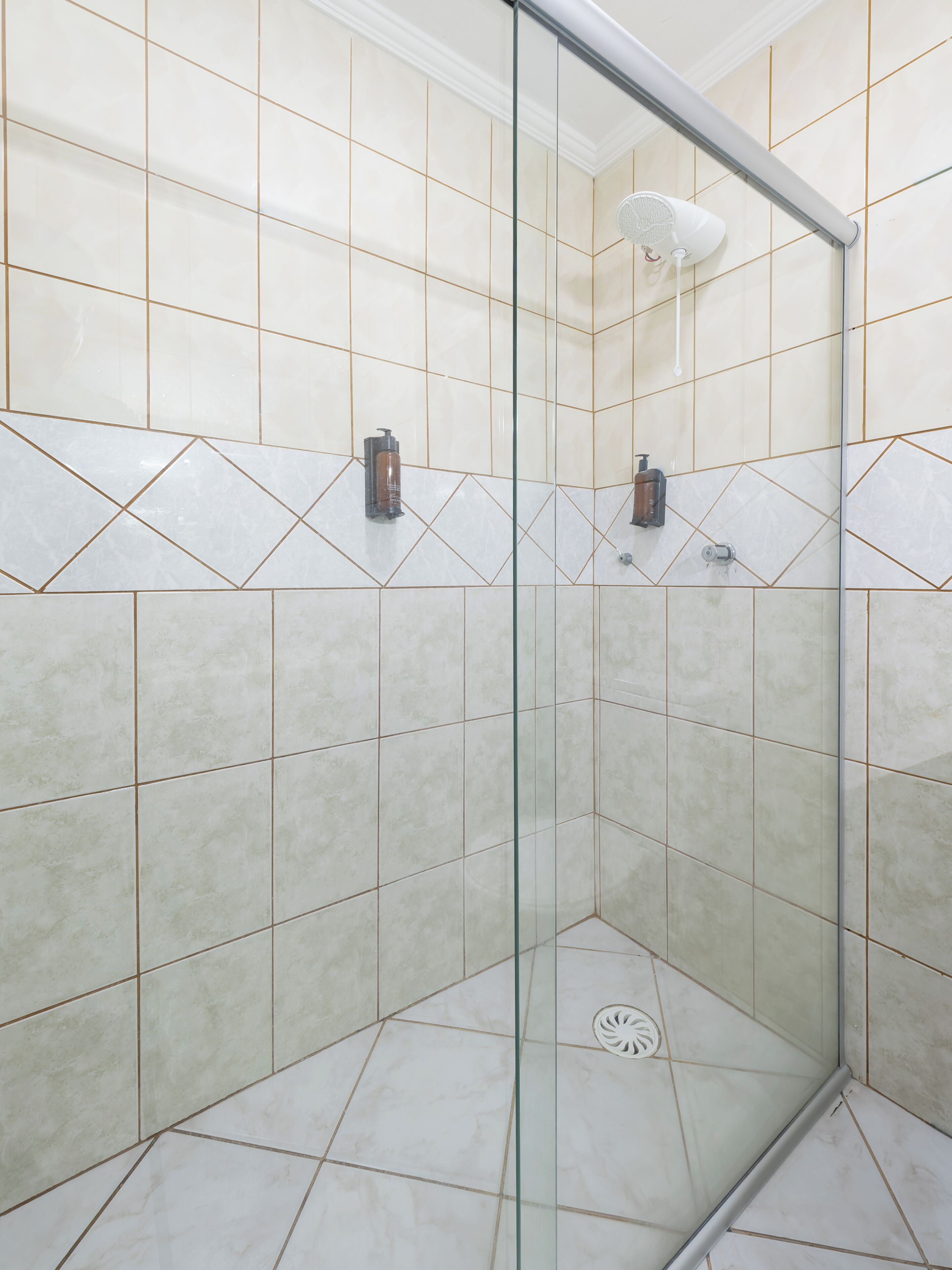 Ducha con puerta de vidrio, paredes de azulejos y ducha de mano.