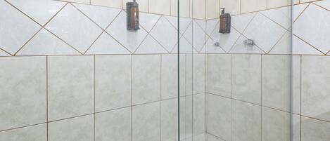 Ducha con puerta de vidrio, paredes de azulejos y ducha de mano.