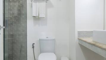 Un bany amb box de dutxa de vidre, un vàter, un lavabo amb taulell de marbre i un terra de rajoles blanques.