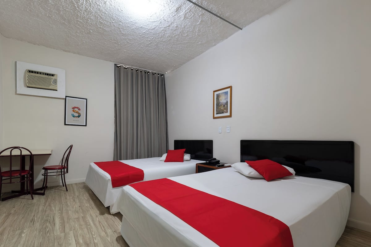 Camera d'albergo con due letti, una scrivania, una sedia, un quadro e una ventola a soffitto.