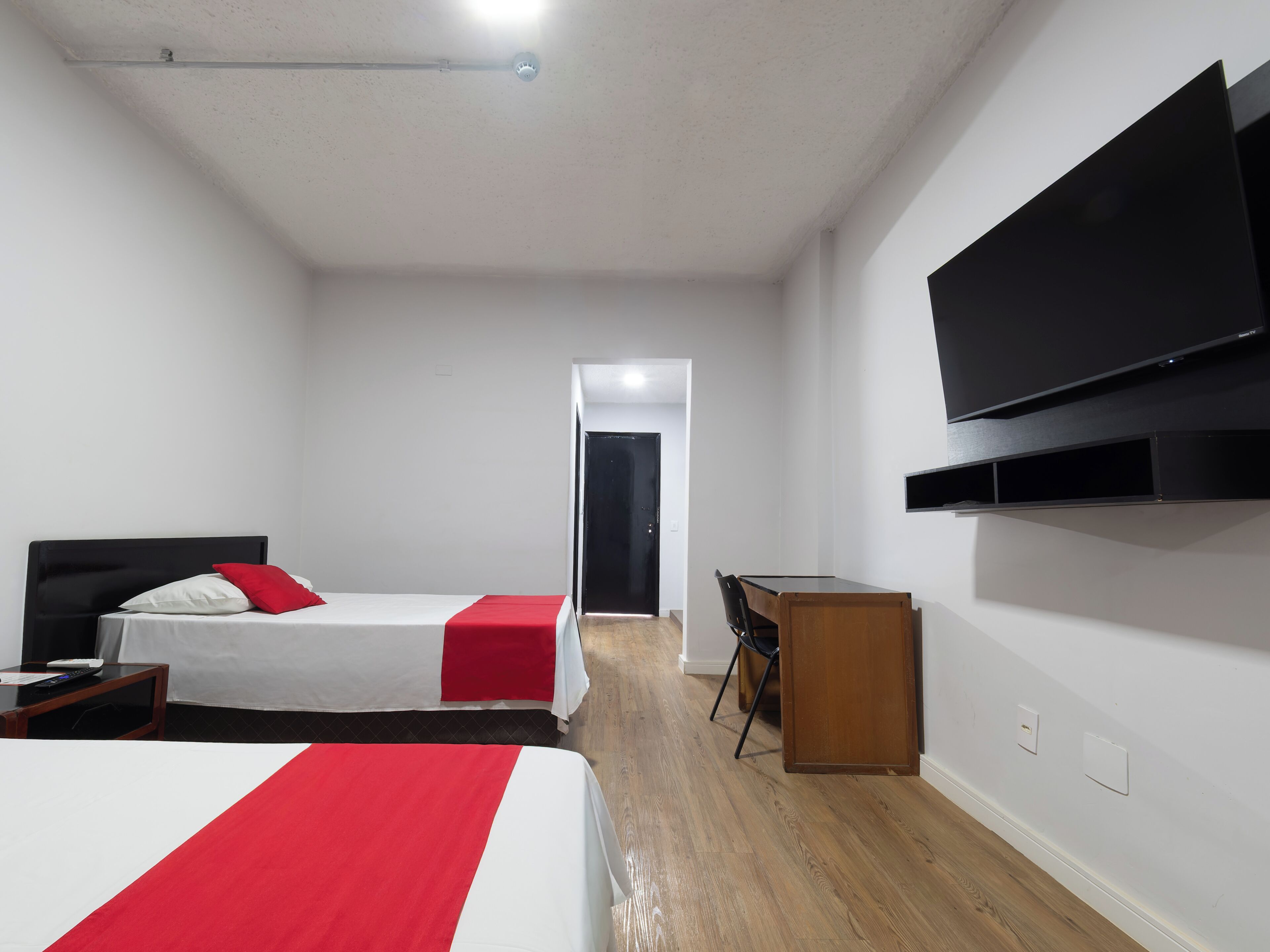 Hotellihuone, jossa on sänky, työpöytä, tuoli, televisio ja ovi, joka johtaa toiseen huoneeseen.