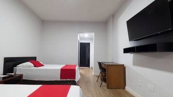 Hotellihuone, jossa on sänky, työpöytä, tuoli, televisio ja ovi, joka johtaa toiseen huoneeseen.